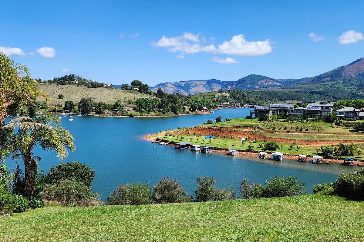 A scenic elevated view overlooking a large lake, surrounding hills, and distant mountains, showcasing the natural landscape and waterfront setting.