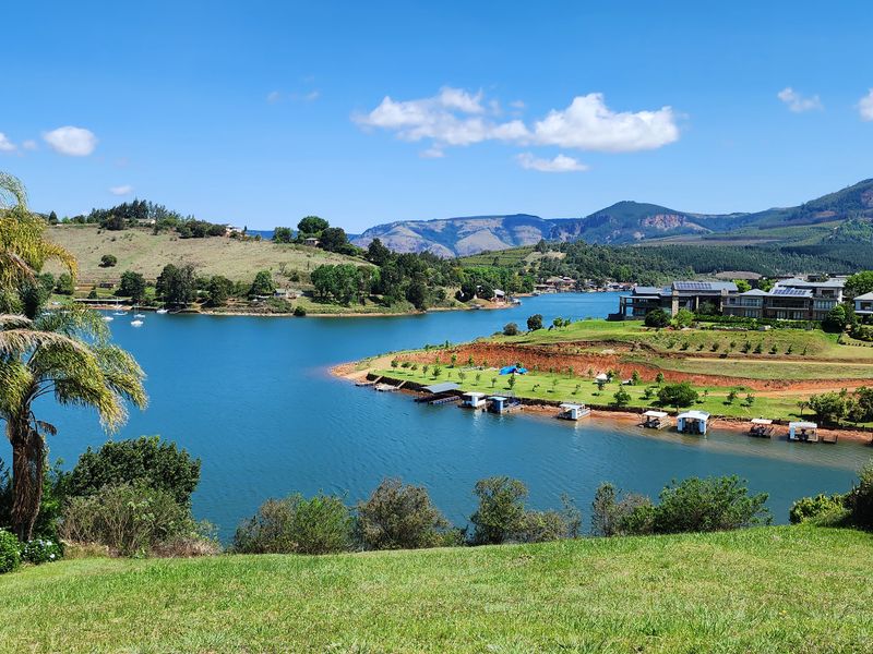 A scenic elevated view overlooking a large lake, surrounding hills, and distant mountains, showcasing the natural landscape and waterfront setting.