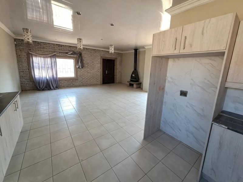Spacious open-plan living area featuring tiled floors, an exposed brick feature wall, and a modern freestanding fireplace, seamlessly connected to the kitchen area.