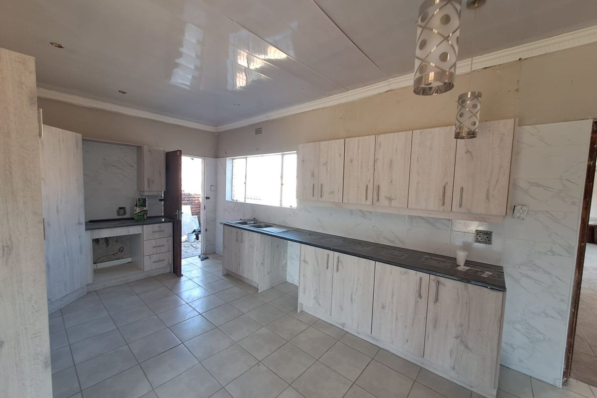A spacious kitchen featuring light wood-finish cabinetry, dark countertops, tiled flooring, and a tiled backsplash, currently awaiting final appliance installation and finishing touches.