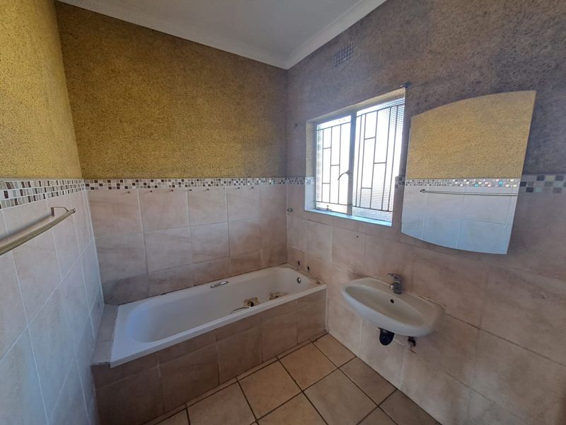 A functional bathroom featuring a built-in bathtub, wall-mounted basin, and tiled finishes, currently awaiting updates to fixtures and decor.
