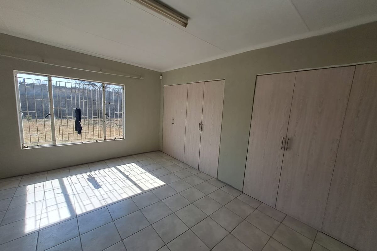 A vacant bedroom featuring tiled flooring, built-in cupboards, and a window with security bars, offering a blank canvas for potential updates.