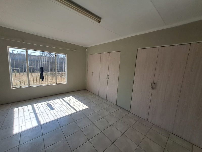 A vacant bedroom featuring tiled flooring, built-in cupboards, and a window with security bars, offering a blank canvas for potential updates.