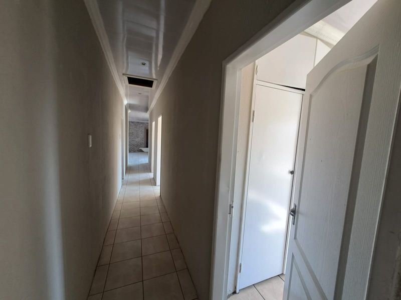 A long, empty hallway featuring tiled flooring, glossy ceiling finishes, and built-in storage cupboards, currently in a state of partial completion.