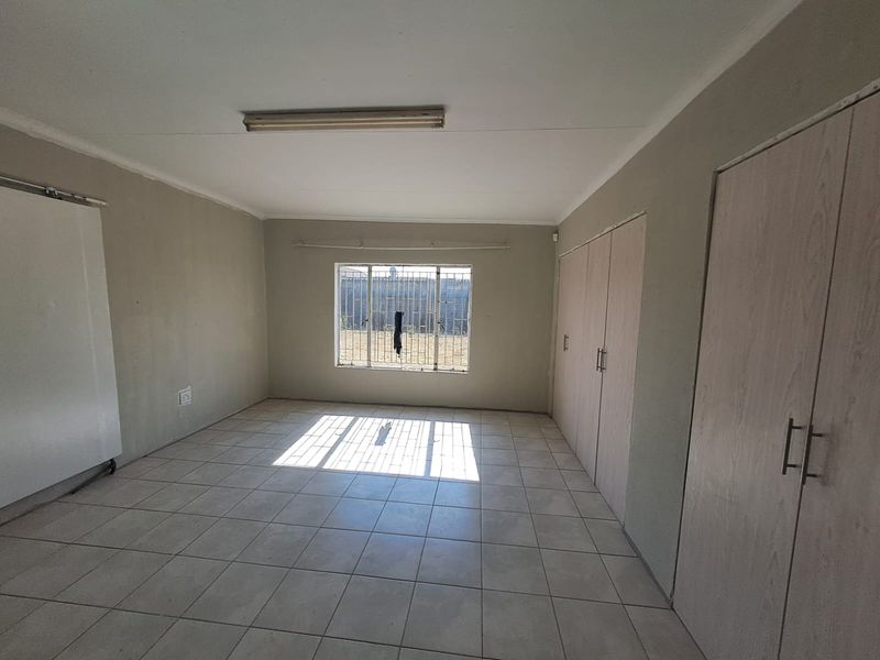 An empty bedroom featuring tiled flooring, built-in cupboards, and a window with security bars, offering a blank canvas for potential updates.