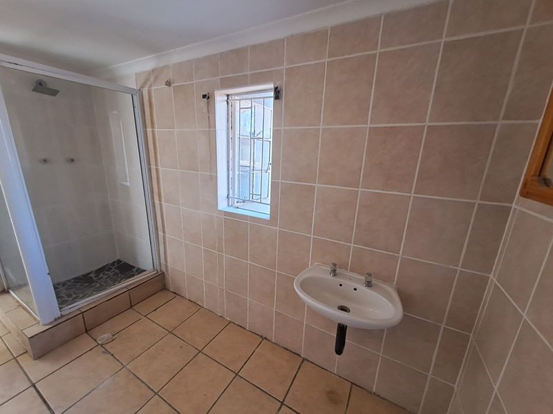 A functional bathroom featuring a shower enclosure, wall-mounted basin, and tiled finishes, currently requiring maintenance and cosmetic updates.