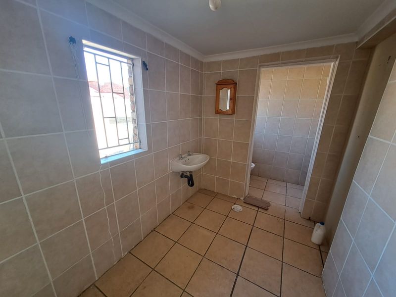 A basic, tiled bathroom featuring a wall-mounted basin and an adjoining toilet area, requiring cosmetic updates to improve its overall condition.