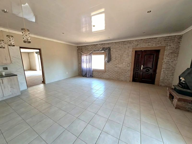 Spacious open-plan living area featuring tiled floors, an exposed brick feature wall, and a built-in wood-burning fireplace.