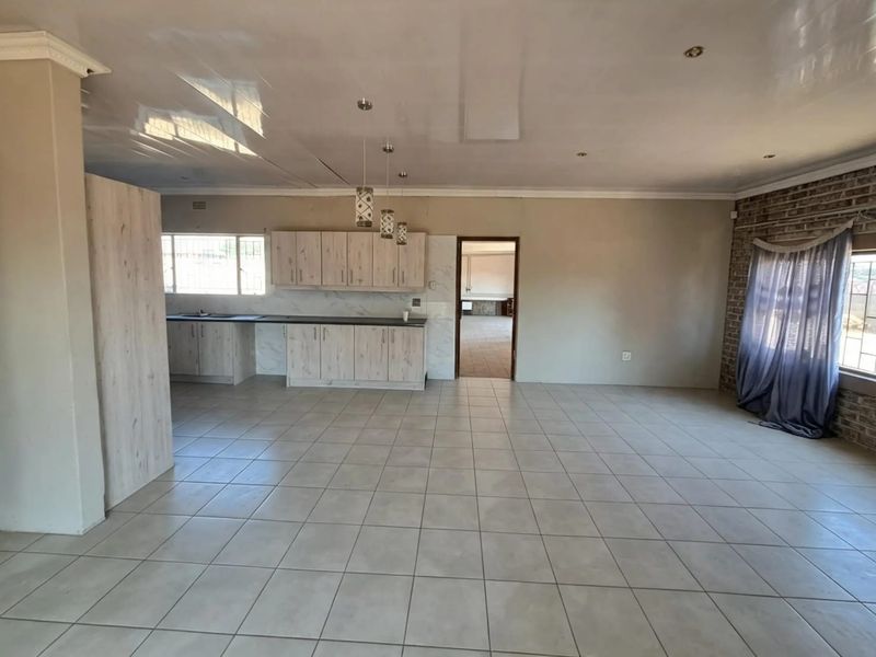 Spacious open-plan living and kitchen area featuring light wood-finish cabinetry, neutral tiled flooring, and an exposed brick feature wall.