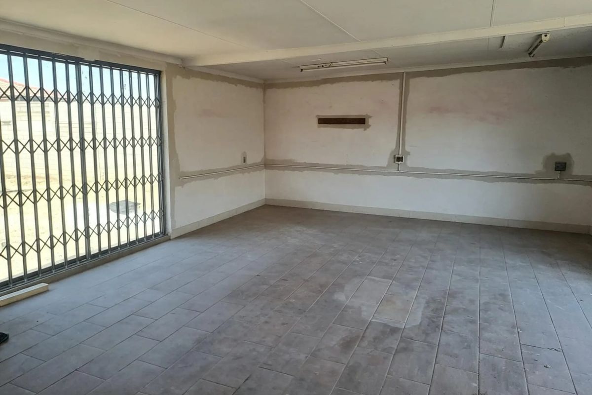 An empty, unfinished living area featuring tiled flooring, security gate, and exposed wall surfaces, offering a blank canvas for renovation.