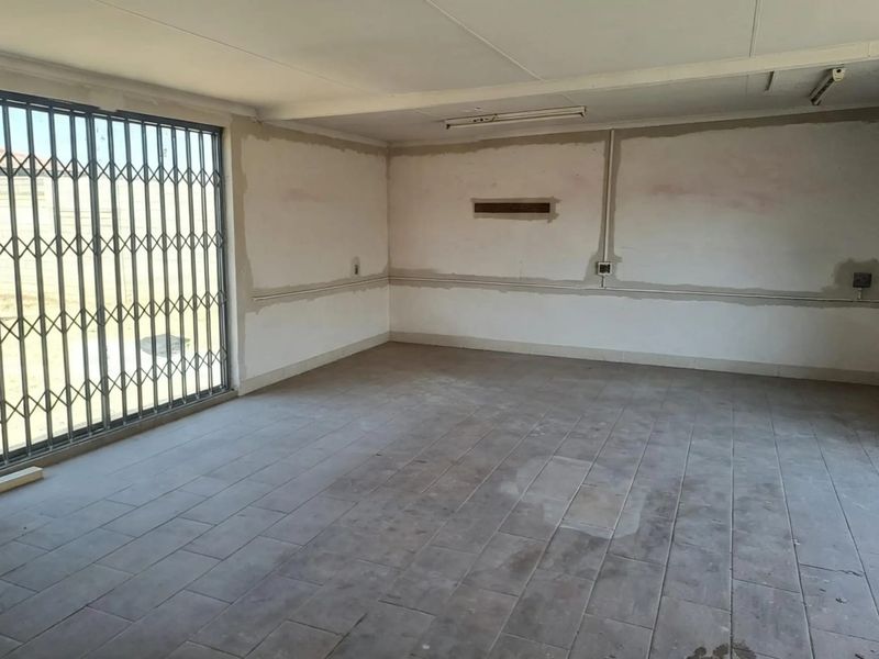 An empty, unfinished living area featuring tiled flooring, security gate, and exposed wall surfaces, offering a blank canvas for renovation.