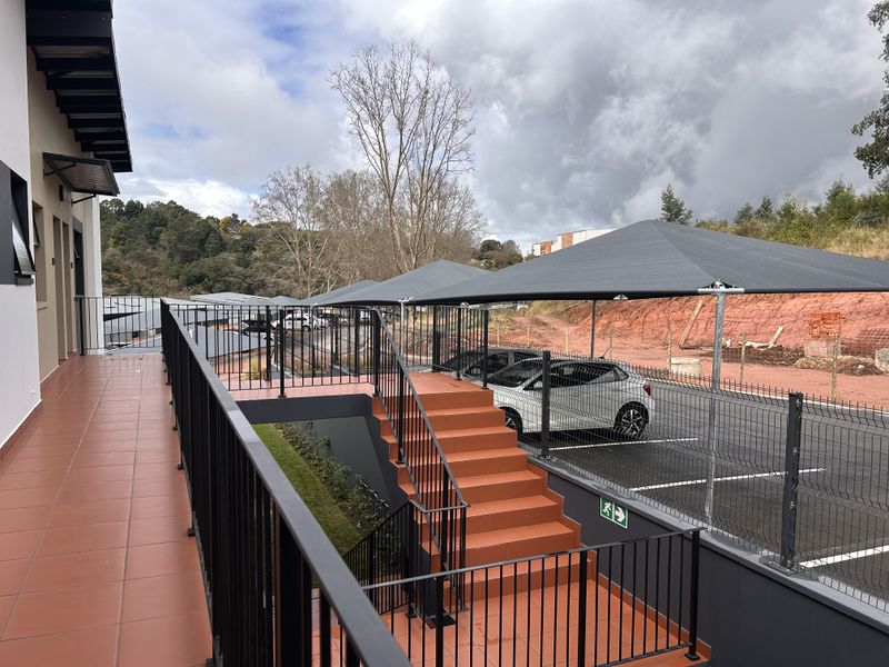 Exterior view of an apartment complex featuring a tiled walkway, metal staircase, and covered parking bays with shade cloth structures.