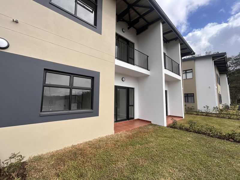 Rear view of a modern apartment building featuring private balconies, terracotta tiled patios, and large aluminium-framed windows overlooking a landscaped garden area.