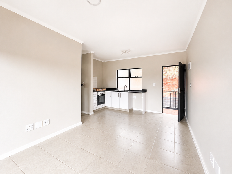 Bright open-plan kitchen and living area featuring neutral tiled flooring, modern cabinetry, built-in oven, and direct access to an outdoor space.