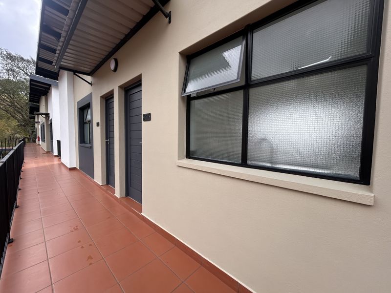 A clean, well-maintained apartment balcony featuring terracotta-style floor tiles, black-framed windows with textured glass, and a secure metal balustrade.