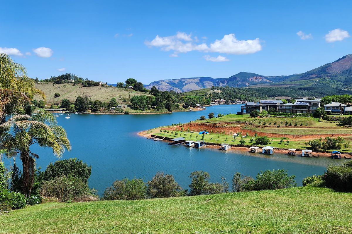 A scenic elevated view overlooking a large lake, surrounding hills, and distant mountains, showcasing the natural landscape of the residential estate.