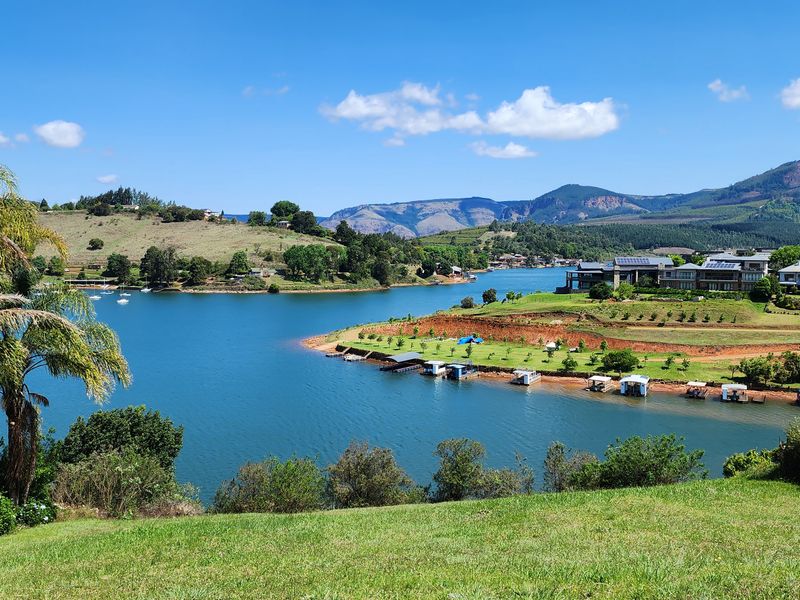 A scenic elevated view overlooking a large lake, surrounding hills, and distant mountains, showcasing the natural landscape of the residential estate.