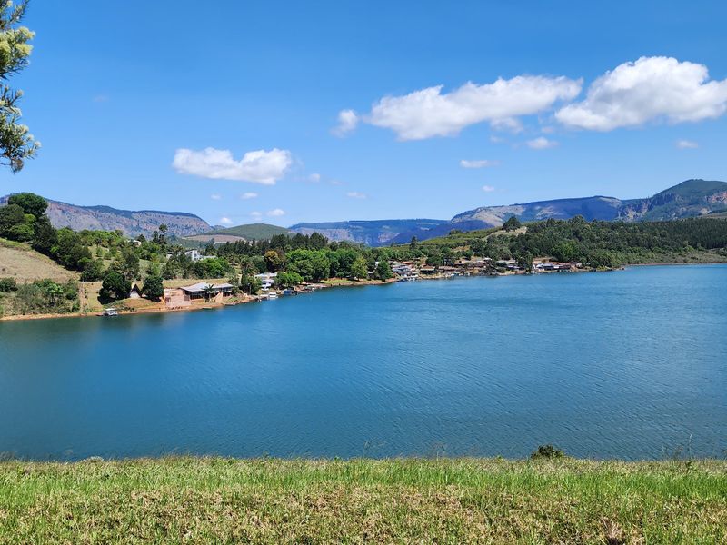 A scenic panoramic view of a large lake surrounded by rolling hills and distant mountains under a clear blue sky.