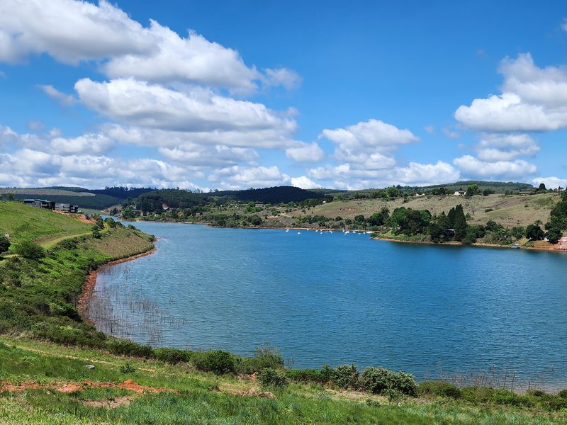 A scenic panoramic view of a large dam or lake surrounded by rolling green hills and natural landscape.