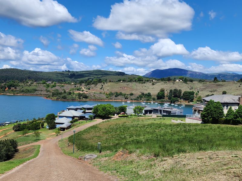A scenic elevated view overlooking a tranquil lake, surrounding hills, and established residential estate properties.