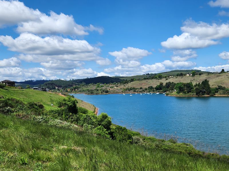A scenic view of a large lake surrounded by rolling green hills and residential properties in the distance.