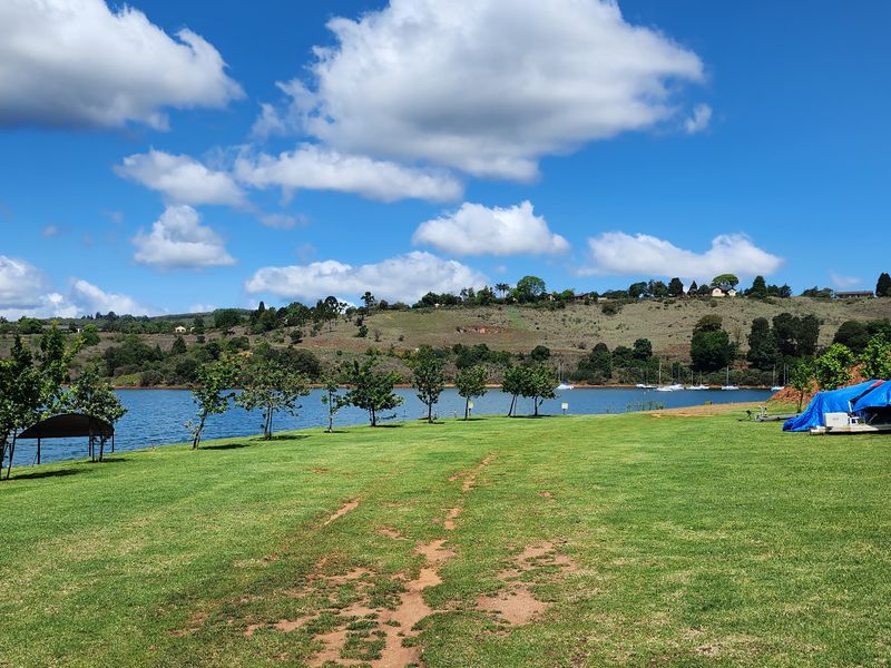 A scenic view of the waterfront property featuring a well-maintained grass lawn, mature trees, and direct access to the lake.