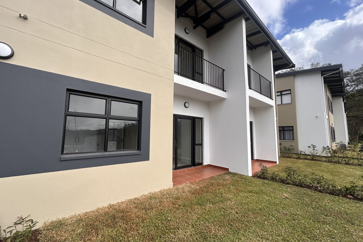 Rear view of a modern apartment building featuring private balconies, terracotta tiled patios, and large aluminium-framed windows overlooking a landscaped garden area.