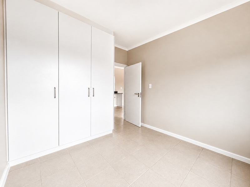 A bright, empty bedroom featuring neutral wall tones, tiled flooring, and ample built-in cupboard storage space.