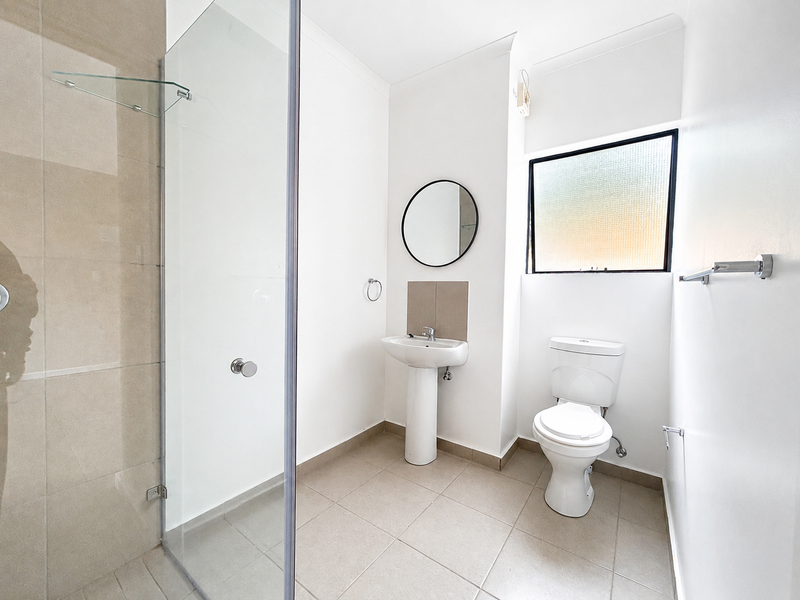 A clean and well-maintained bathroom featuring a glass-enclosed shower, pedestal basin, and toilet with neutral floor tiling and bright white walls.