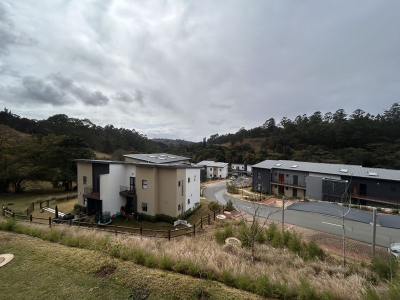 An elevated aerial view of a modern apartment complex development set within a scenic, natural landscape with paved access roads.