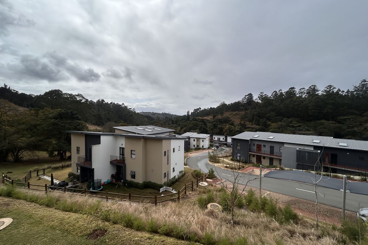 An elevated aerial view of a modern apartment complex development set within a scenic, natural landscape with paved access roads.
