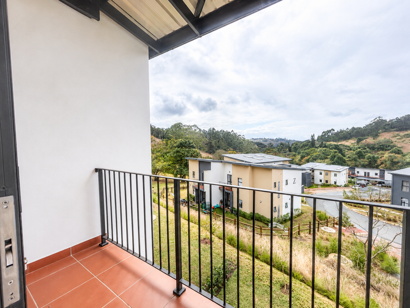 A clean, covered balcony featuring tiled flooring and a metal balustrade, offering elevated views of the surrounding residential estate and landscape.