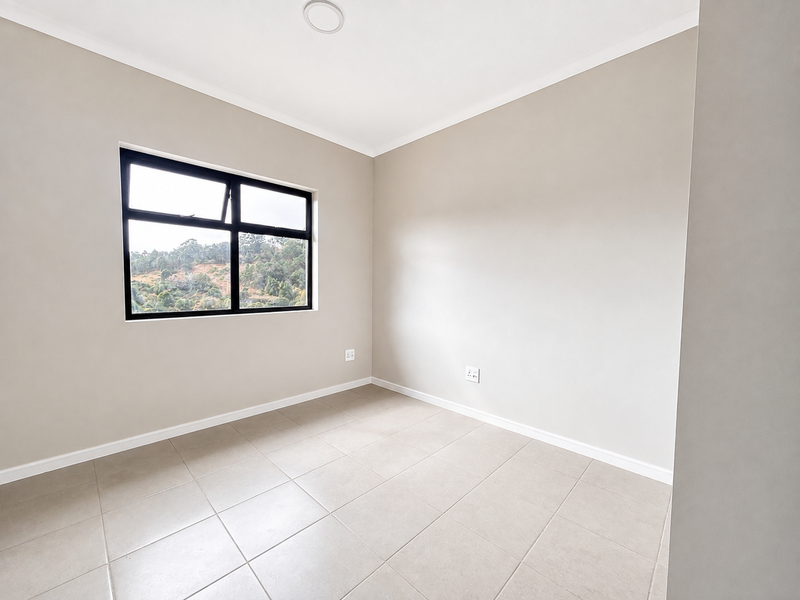 A bright, empty bedroom featuring neutral tiled flooring, clean walls, and a black aluminium window frame with a scenic view.