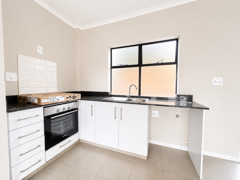 A clean, modern kitchen featuring white cabinetry, granite countertops, a built-in oven, and a subway tile backsplash with neutral floor tiling.