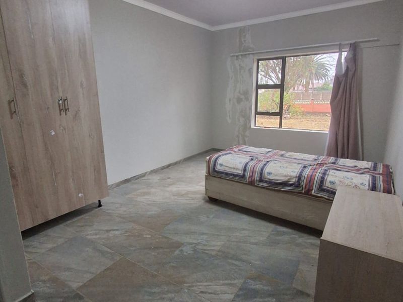 A bedroom featuring tiled flooring, a built-in wardrobe, and a window with visible water damage on the surrounding wall.