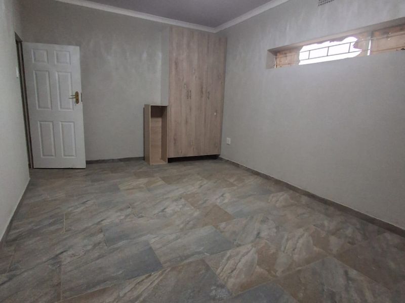 An empty bedroom featuring tiled flooring, a built-in wardrobe, and a high-level window, providing a neutral space ready for personalization.