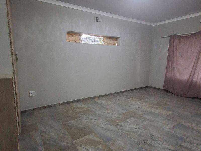 An empty bedroom featuring tiled flooring, a built-in cupboard, and a ceiling light fixture, with an unfinished window opening requiring attention.