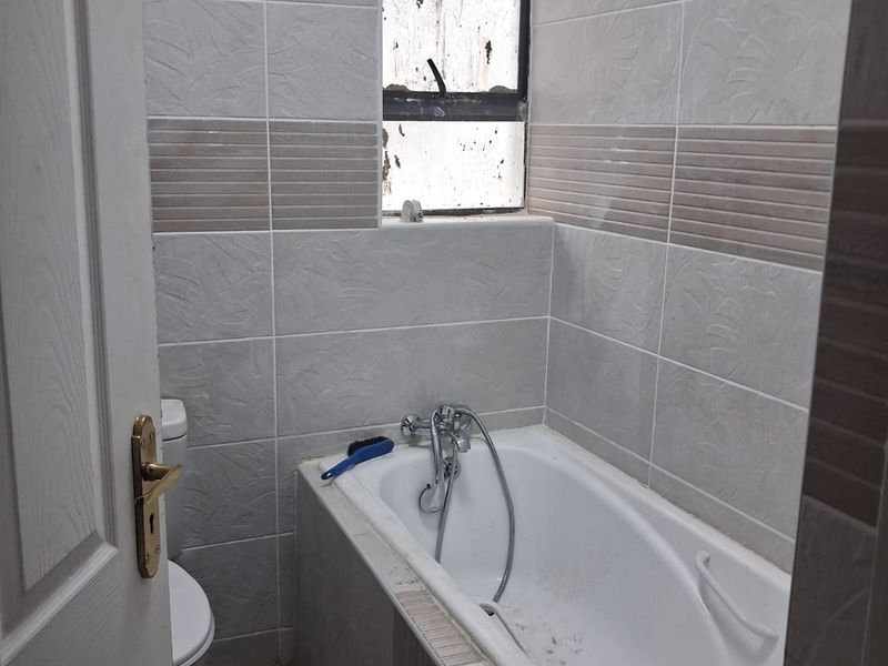 A compact bathroom featuring a bathtub with a shower mixer, toilet, and tiled wall finishes.