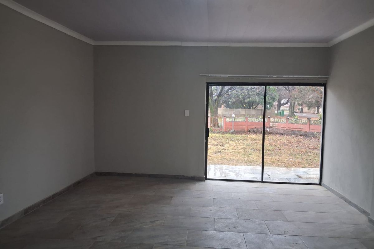 A spacious, empty living room featuring neutral tiled flooring and a large sliding glass door providing access to the rear garden.