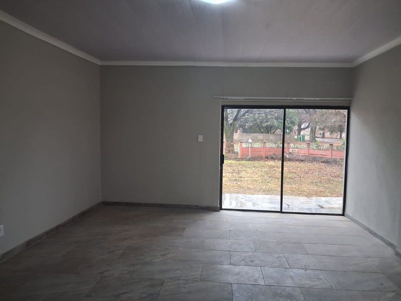 A spacious, empty living room featuring neutral tiled flooring and a large sliding glass door providing access to the rear garden.