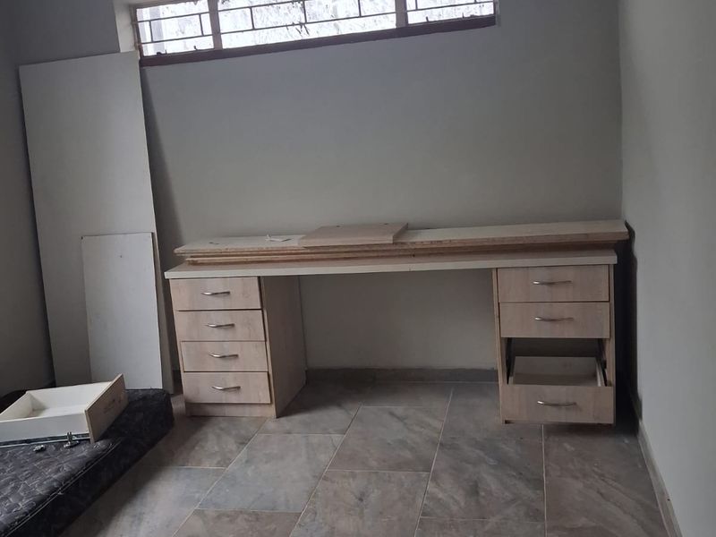 A bedroom featuring tiled flooring, a high-set window with security bars, and a built-in desk unit requiring completion and repair.