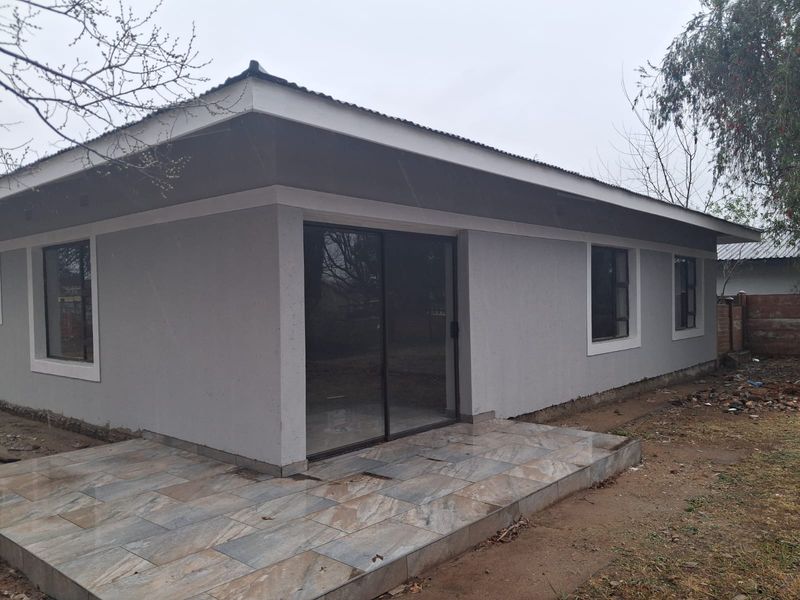 Rear view of the property featuring a tiled patio, sliding glass doors, and modern grey exterior finishes with aluminium window frames.