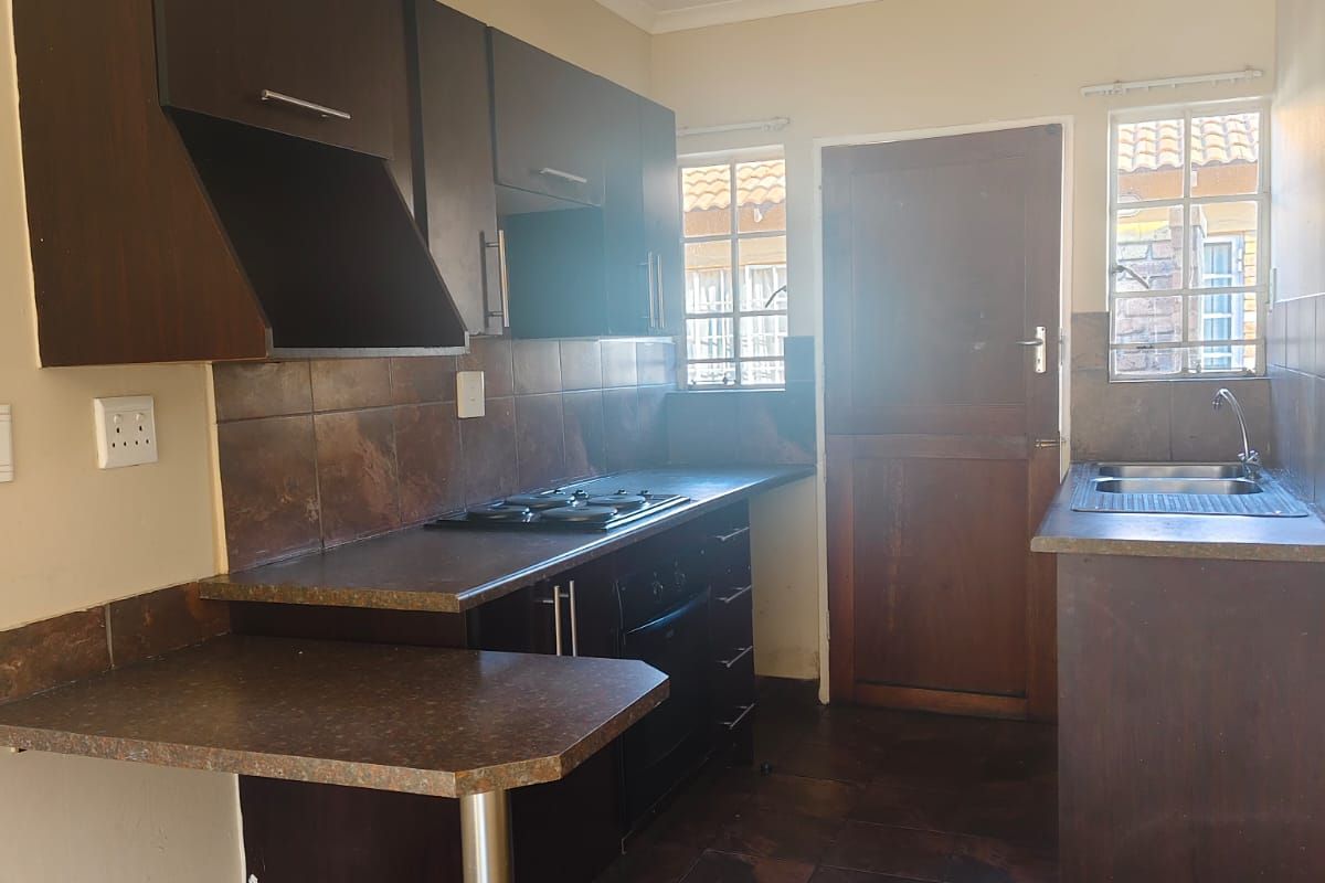 Functional kitchen featuring dark wood cabinetry, gas hob, built-in oven, and tiled finishes, offering a practical layout for daily meal preparation.
