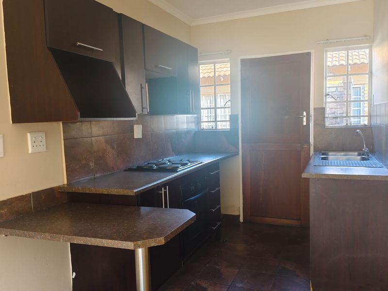 Functional kitchen featuring dark wood cabinetry, gas hob, built-in oven, and tiled finishes, offering a practical layout for daily meal preparation.