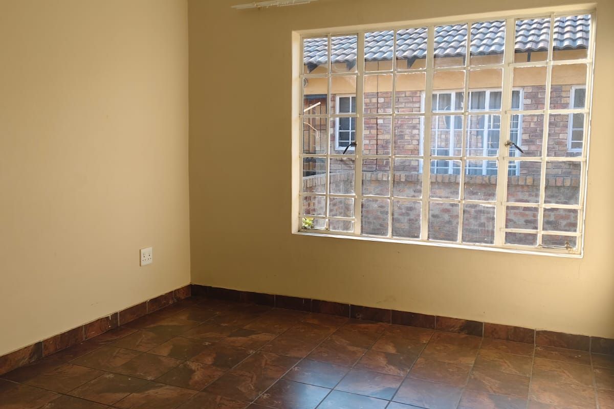 A bright, empty bedroom featuring tiled flooring, a large multi-pane window with a curtain rail, and neutral wall finishes.