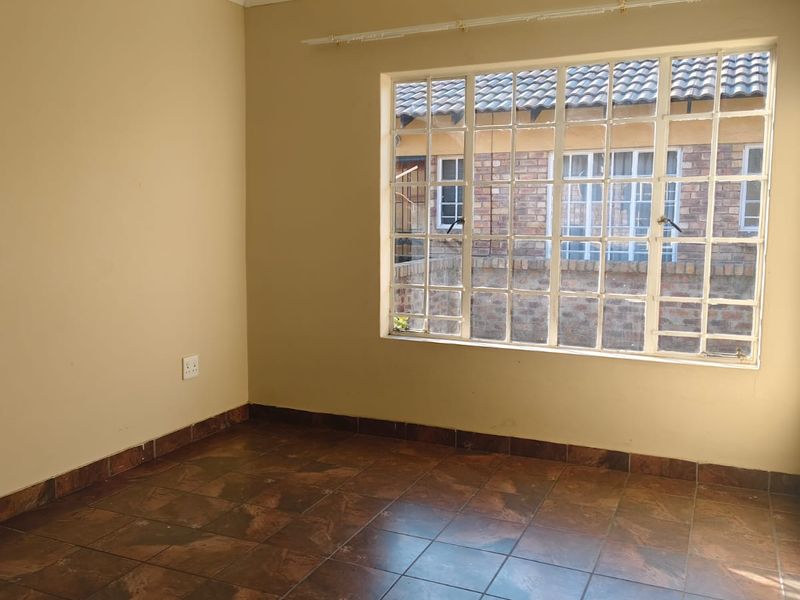 A bright, empty bedroom featuring tiled flooring, a large multi-pane window with a curtain rail, and neutral wall finishes.