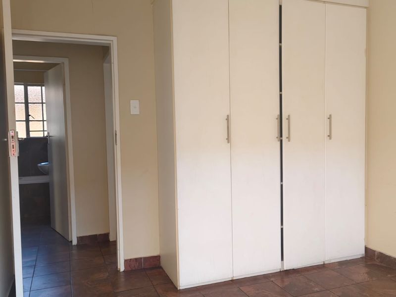 A vacant bedroom featuring built-in cupboards, tiled flooring, and direct access to an adjoining bathroom.