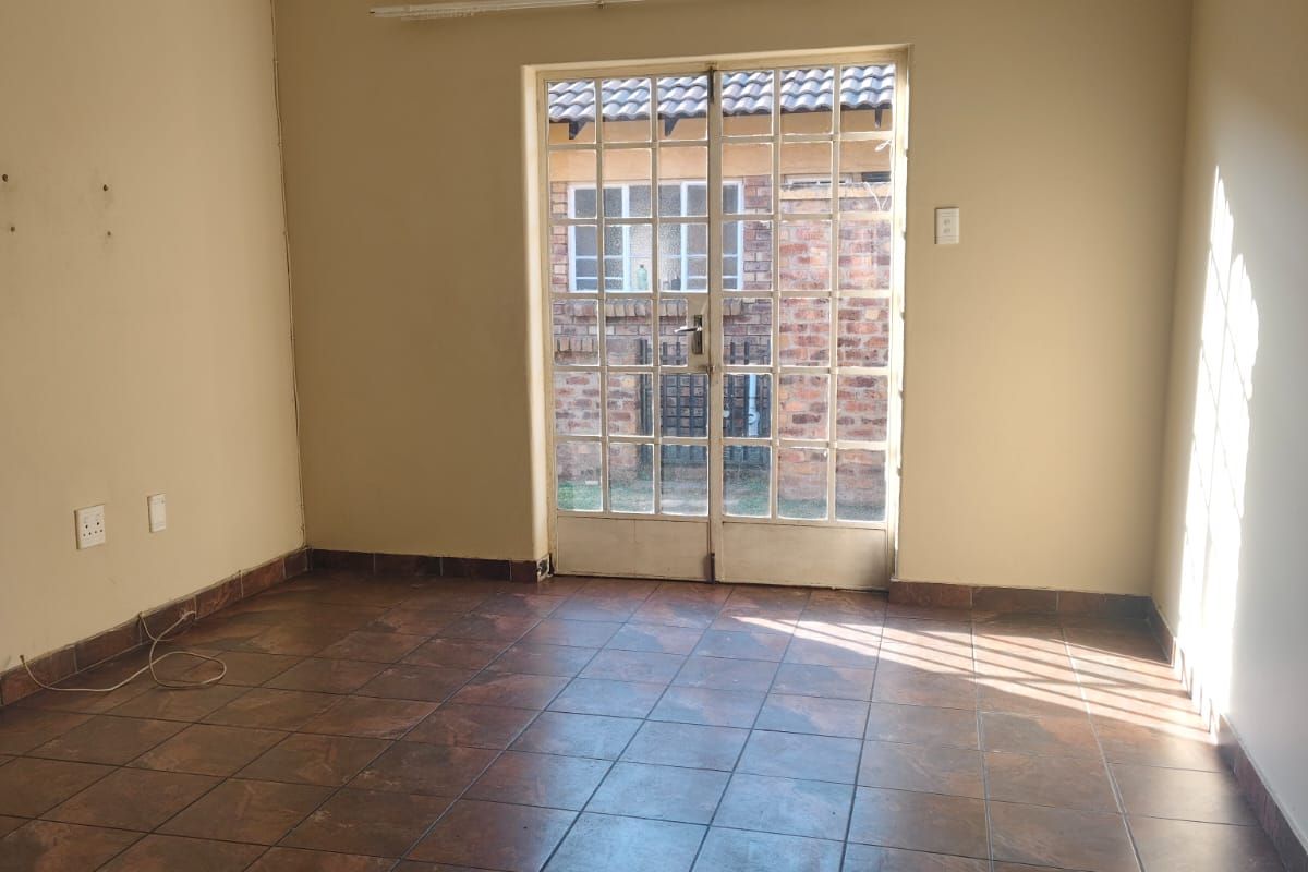 An empty living room featuring tiled flooring and a double glass door providing access to the exterior.