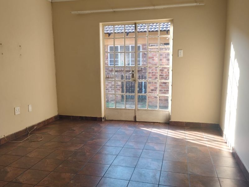 An empty living room featuring tiled flooring and a double glass door providing access to the exterior.