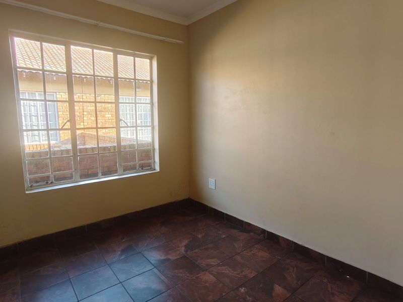 An empty bedroom featuring dark tiled flooring, a large window with security bars, and neutral wall finishes.